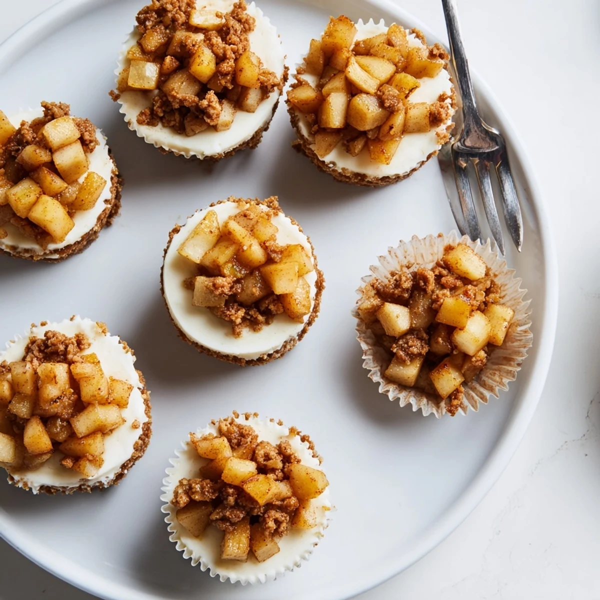 Delicious apple crisp mini cheesecakes displayed on serving platter with graham cracker crust and fruit crisp garnish