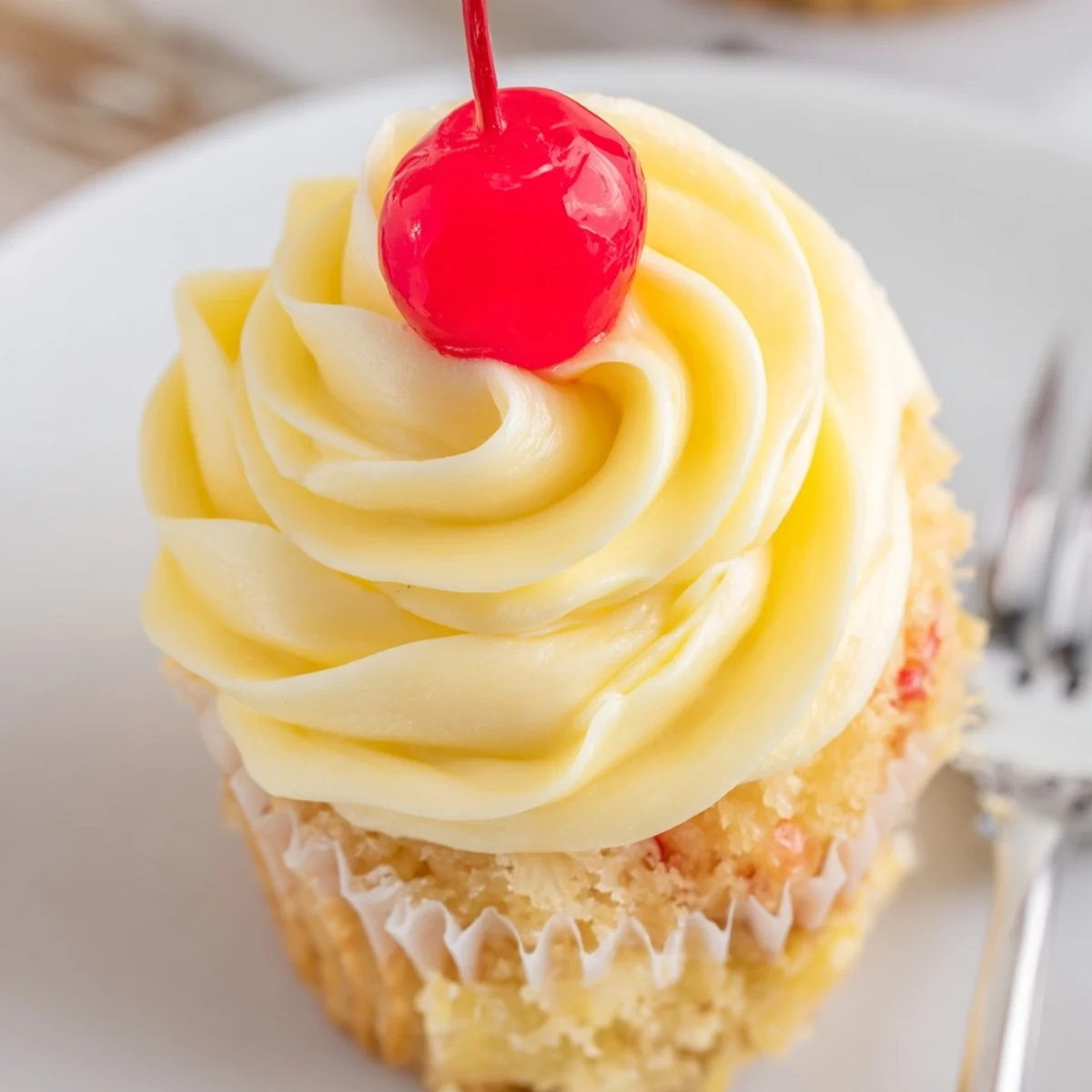 Golden Dole Whip Cupcakes topped with creamy pineapple whipped frosting and cherry garnish