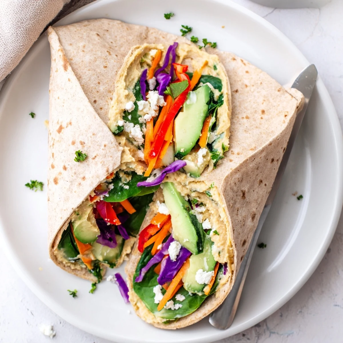 Colorful vegetable wrap packed with baby spinach shredded carrots bell peppers and smooth hummus spread on spinach tortilla