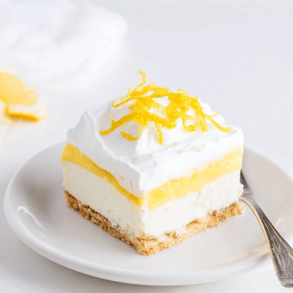 Close-up of lemon lush cake rectangle with buttery crust tangy pudding layer and billowy white whipped topping on serving plate