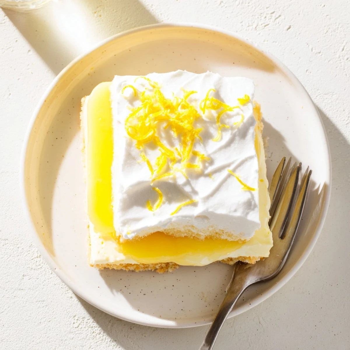Golden lemon lush cake sliced square showing creamy layered dessert topped with fluffy whipped cream and bright lemon zest garnish