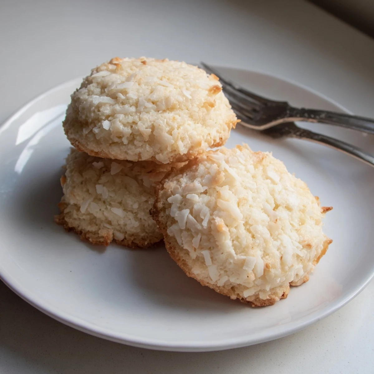 Golden coconut cookies with crispy edges and soft chewy centers on a rustic baking sheet