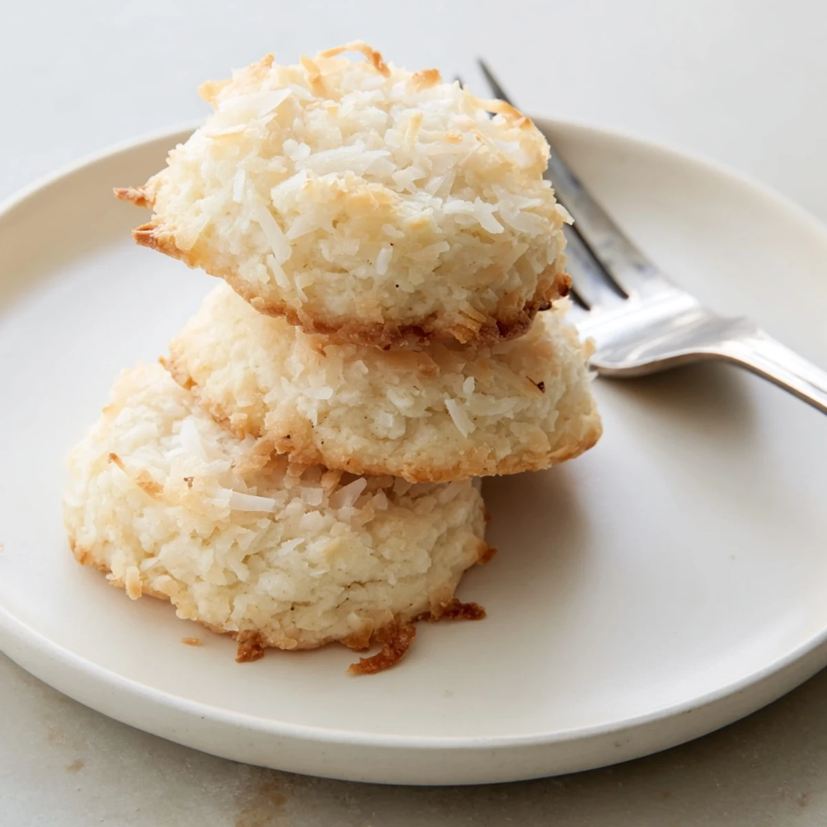 Soft and buttery coconut cookies stacked on a plate dusted with powdered sugar