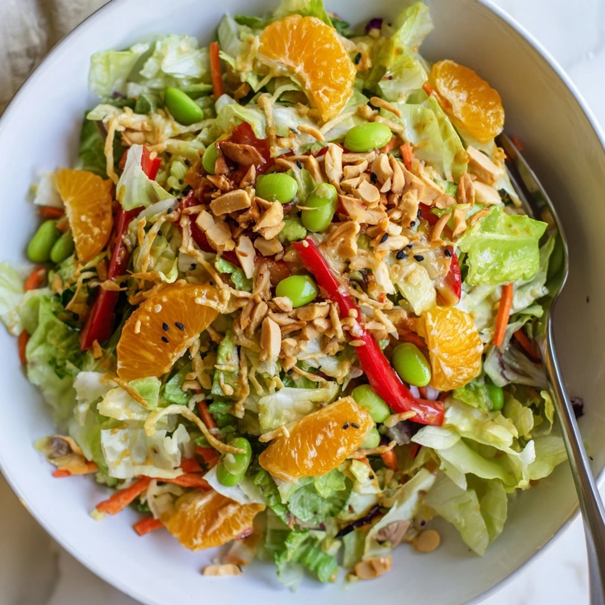 Bright Mandarin Sesame Crunch Salad topped with golden noodles and toasted almonds in a glossy bowl